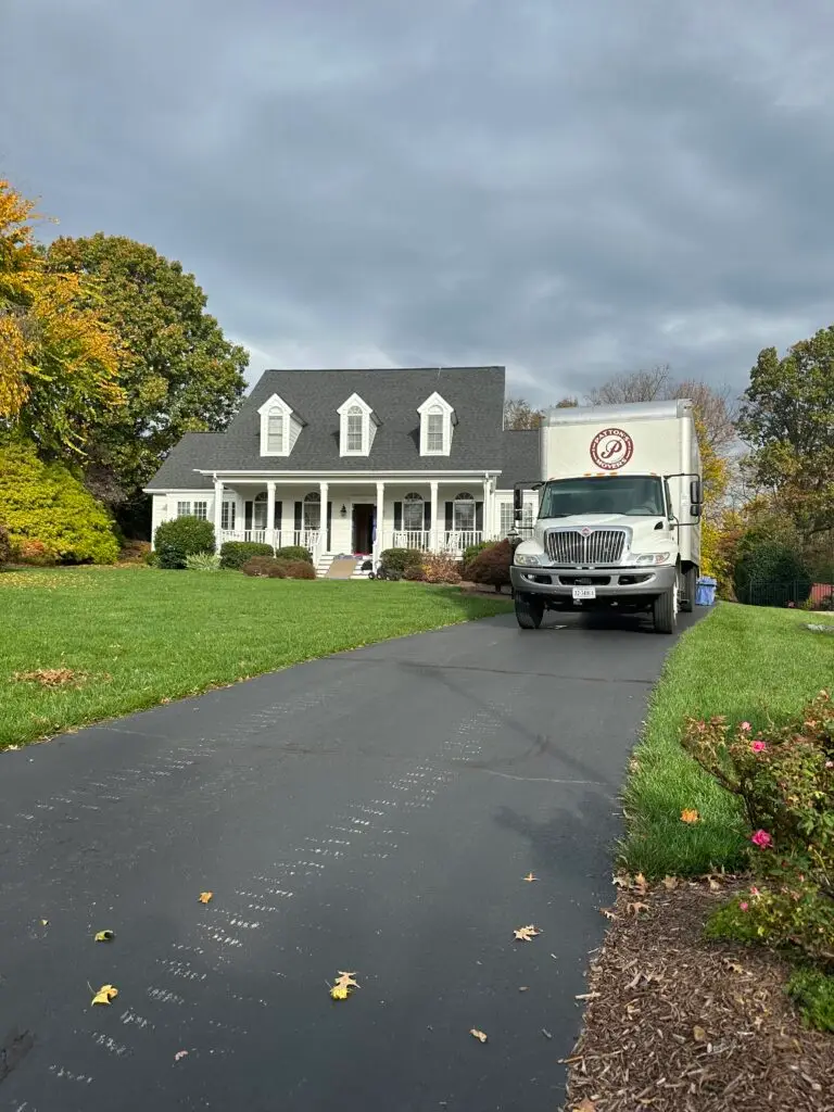Patton's Movers truck parked in front of a beautiful white house with a manicured lawn, ready for a local residential move in Winchester, VA.